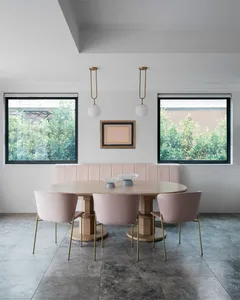Modern dining room featuring a round table with metal legs, upholstered pink chairs, and a contemporary bench seat.