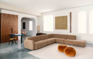 Modern living room with a beige fabric sectional sofa, two orange poufs, and a tall lamp on a low table, set against a white 
