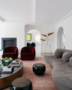 A modern living room with a velvet upholstered sofa, a round wooden coffee table, a black and white marble side table, and a