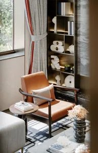 A modern living room featuring a leather armchair, a side table with stacked books, and a bookshelf with decorative items.