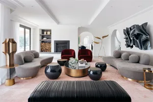 Modern living room featuring grey sofas, red accent chairs, and black side tables, with a fireplace and large windows.
