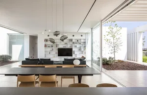 A modern living room featuring glass walls, a black table, and a white shelving unit with books and decor.