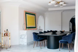 Modern minimalist dining room with a marble table and chairs, a bar cart, and a large colorful abstract painting on the wall.