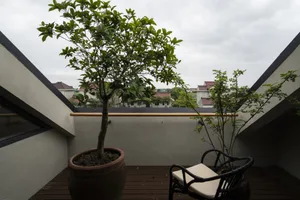 A modern balcony with potted plants, wooden floor, and a seat.