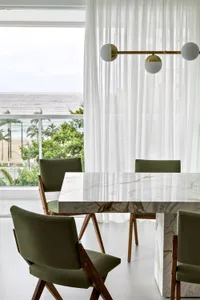 Modern dining room with marble table and green chairs, overlooking the ocean.
