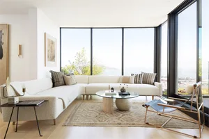 Modern living room with a white sectional couch, glass coffee table, and floor-to-ceiling windows overlooking a scenic landsc