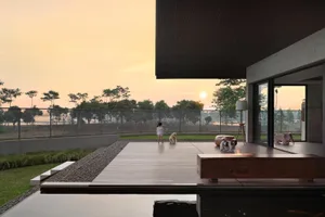 A minimalist patio area featuring a wooden deck and furniture, with a child and dogs in the background at sunset.