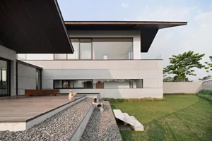 Modern house with concrete exterior, glass windows, and dogs on a gravel path leading to the front door.