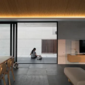 A modern residential interior with a minimalist design, featuring exposed concrete walls and floor tiles, natural light, and