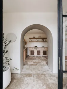 A minimalist entryway featuring a tile floor, wooden cabinets, and a simple, arch-shaped doorway.