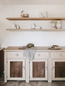 A minimalist kitchen with white cabinets and wooden accents, featuring decorative ceramics on shelves.