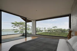 Modern bedroom with glass walls overlooking a serene lake with a grassy landscape.