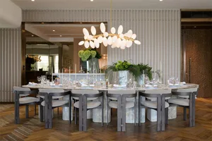 A contemporary dining room with a modern chandelier, marble table, and plush chairs.