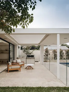 Modern outdoor kitchen and garden with tiled flooring and white outdoor furniture.