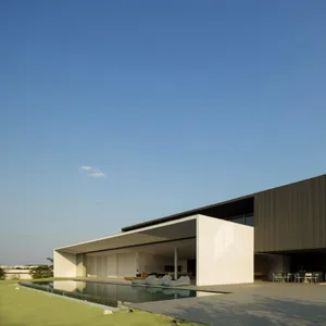 Modern white concrete residential home exterior with large glass walls and swimming pool.