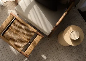 A minimalistic sofa with a wooden frame and cushions, placed next to a round wooden side table with a bowl on top, under a wi