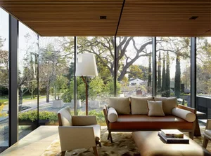 A modern living room featuring wooden walls and a brown leather sofa, with a large window showcasing a serene outdoor landsca