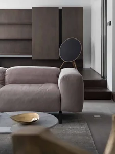 A minimalist living room featuring a beige fabric sofa, wooden cabinets, and a round metal coffee table.