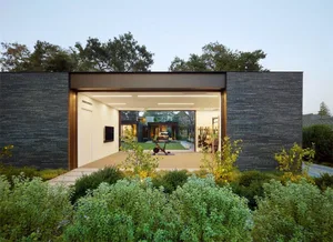 A modern minimalist residential garage with metal walls, glass doors, and stone ground.