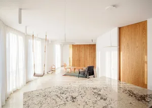 Modern minimalist living room with white marble floor and wooden walls, featuring a swing and a wooden table.