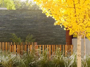 A modern exterior of a building with wooden fences, stone walls, metal accents, and glass windows.