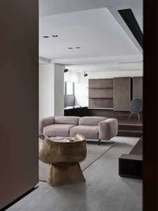 Modern living room with minimalist design featuring a beige sofa, wooden shelves, and a unique metallic side table.