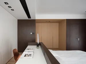 A minimalist bedroom with brown walls, a bed, and a white desk with a desk lamp.