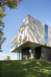 A modern house with smooth concrete walls and large glass windows, viewed from a lower angle.