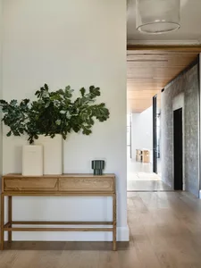 A minimalist interior design featuring a wood console table with a vase and plants, set against a white wall and wooden floor