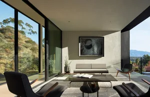 A minimalist living room with concrete walls and a glass window overlooking a scenic landscape.