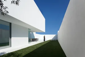 A modern white house with glass walls and a garden.