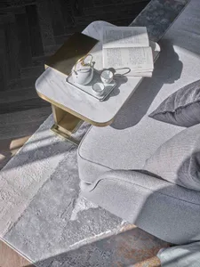 A cozy modern living room featuring a gray sofa, rug, and marble tea table with a teapot and books.