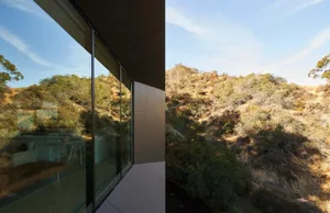Modern exterior of a house featuring large glass windows with a view of a hillside.