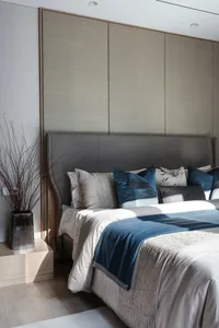 A modern minimalist bedroom featuring a custom upholstered headboard adorned with patterned throw pillows, white bedding, and