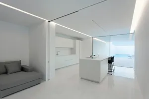 Empty room with modern minimalist design, featuring white walls and floor, minimalist furniture, and a kitchen with a white i