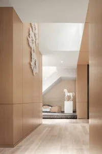 A minimalist modern living room with light-colored wooden walls and floors, and a white horse sculpture on a pedestal.
