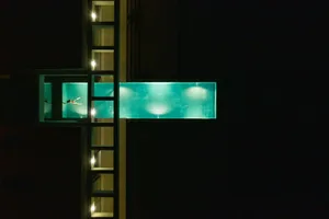 A modern, illuminated glass swimming pool at night with a swimmer inside.