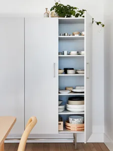 Minimalist kitchen with white ceramic shelves, white and black plates, and a wooden dining table