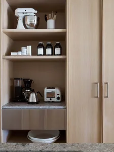 A modern minimalist kitchen with wooden cabinets and a grey countertop, featuring essential appliances like a toaster, kettle