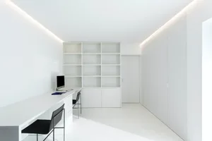 A minimalist office space with white walls, furniture, and shelves.