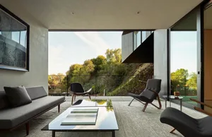A modern living room featuring concrete walls, glass windows, and wooden furniture.