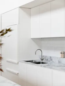 Modern, minimalist kitchen with marble countertops and white cabinets.