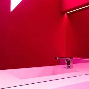 Modern minimalist bathroom with a white sink, faucet, and red lighting.