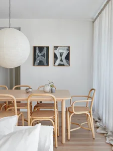 A modern minimalist dining room featuring wooden furniture and light-colored woven chairs.