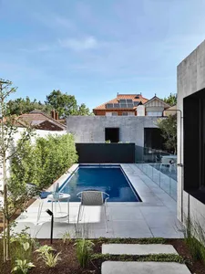 A modern pool deck featuring a rectangular swimming pool bordered by concrete tiles, with a minimalist aesthetic and surround