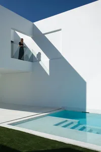A minimalist residential balcony featuring a sleek concrete design and clear blue sky, with a person standing on the balcony.