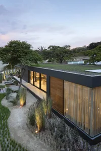 Modern residential house exterior with sand-textured walls and greenery at dusk