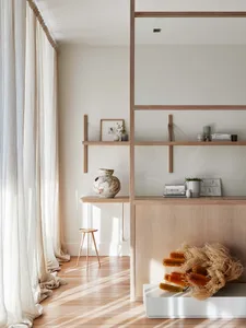 A well-lit, modern residential space featuring wooden shelves, glass doors, ceramic vases, and textile elements.