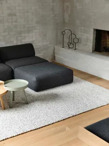 Modern minimalist living room featuring a wool rug, a dark grey modular sofa, a small round table, and a white fireplace with