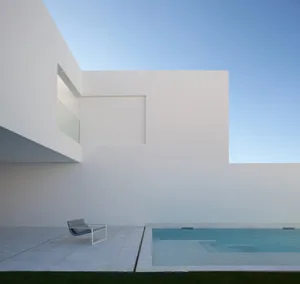 Modern minimalist house with white walls, glass window, and concrete patio and pool.